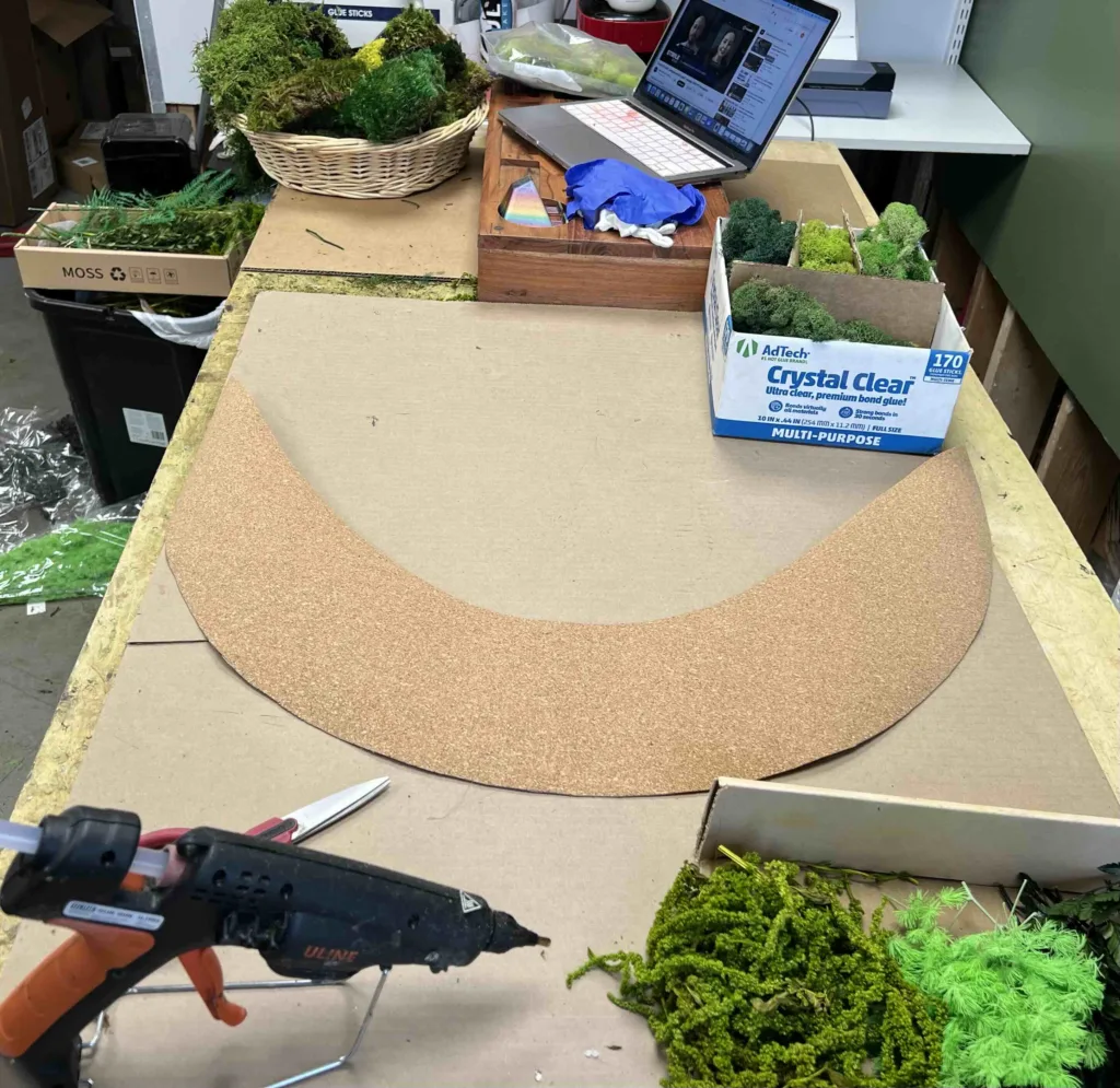 A crescent shape panel on a table with a few boxed of different shades moss around it.