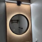 A bathroom with a frame on the wall above the vanity and a round mirror with a wooden frame.